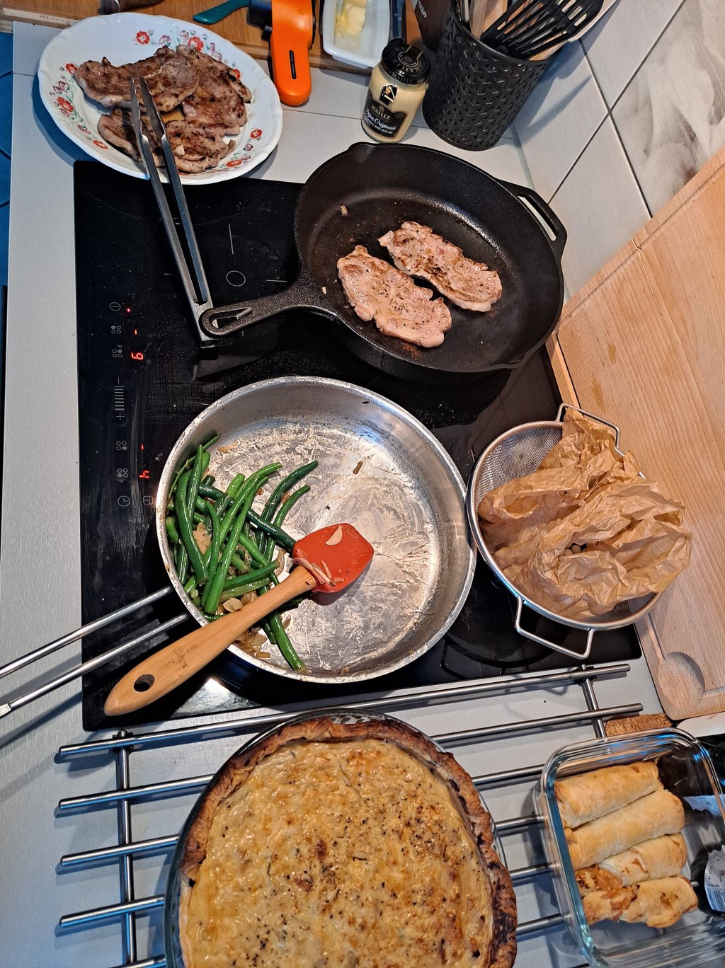 An induction stovetop with pork steaks, sauteed green beans, and an onion quiche.